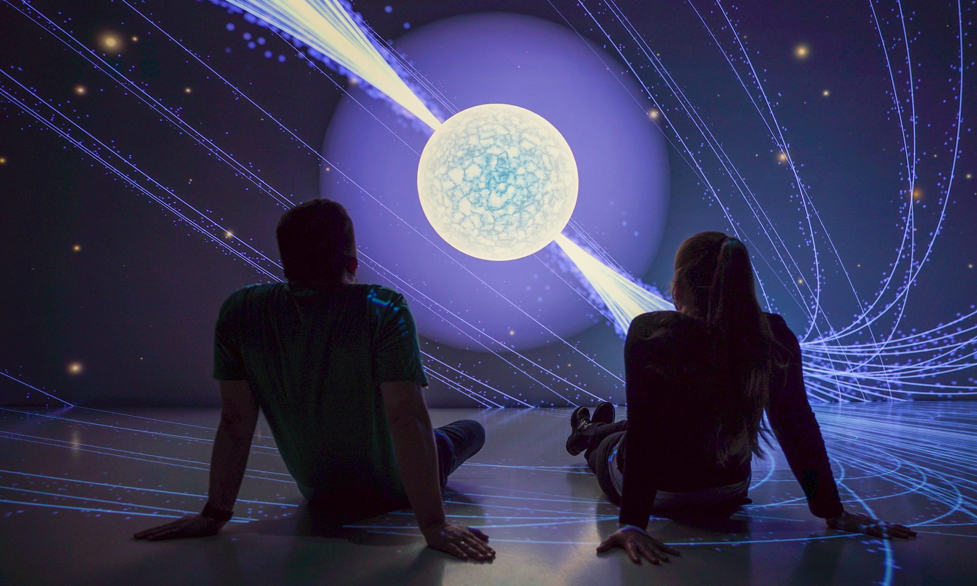 Two people sitting on the floor casually watching a video presentation