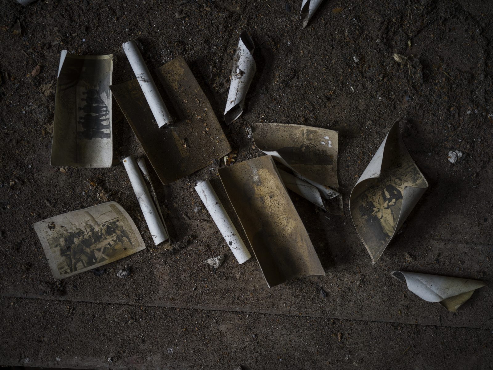 Vanhoja, likaisia, käpristyneita valokuvia likaisella lattialla.