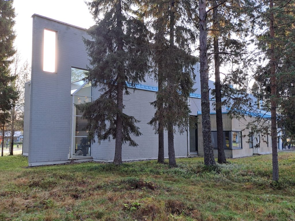 Vaaleatiilinen rakennus, jonka edessä puita.