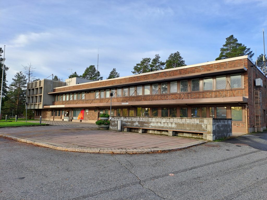 Kaksikerroksinen pitkänmallinen virastorakennus, suurimmaksi osaksi punatiiltä. Paljon ikkunoita.